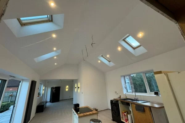 A kitchen part way through installation, with some lights installed and wires hanging down from a high ceiling, ready for more lights to be installed.